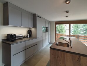 Eine moderne Küche mit grauen Schränken, einem eingebauten Backofen und einem großen Fenster mit Blick ins Freie.