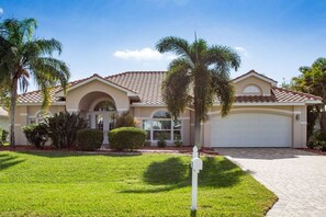 A two-story house with a garage, surrounded by a well-maintained lawn and palm trees. - Villa in Cape Coral with swimming pool (Cape Coral)