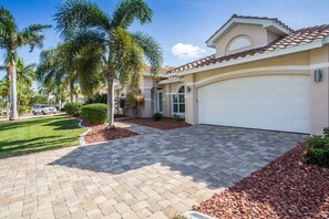 A residential property with a paved driveway, palm trees, and a garage. - Villa in Cape Coral with swimming pool (Cape Coral)