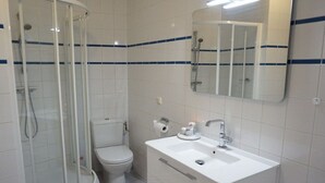Un baño con ducha de vidrio, inodoro, lavabo con espejo y paredes de azulejos blancos.