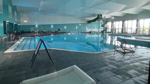 Una piscina interior con vistas claras al área de la piscina, un espacio de descanso y una escalera que conduce a un nivel superior.