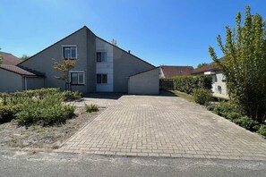 Um edifício residencial de dois andares, com entrada pavimentada e um pequeno jardim.