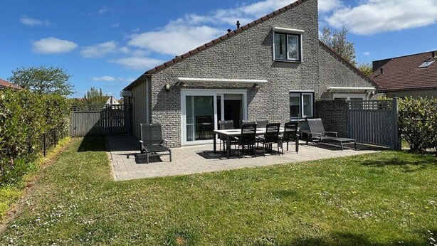 Una casa con fachada de piedra, un patio con mobiliario exterior y un patio trasero cercado.