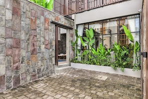 A courtyard with stone walls, a wooden deck, and lush greenery. - Cardano Villa by Kozystay - Canggu (North Kuta, Badung)
