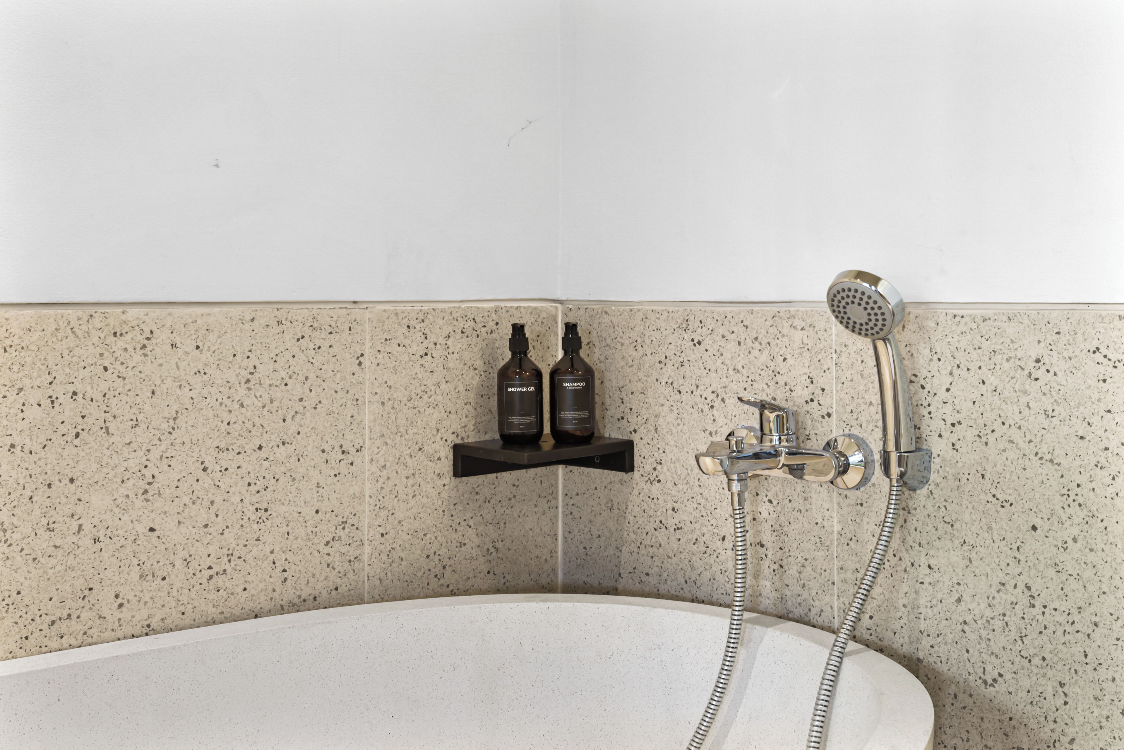 A bathroom with a freestanding bathtub, a handheld showerhead, and two bottles of shower gel and shampoo on a shelf.