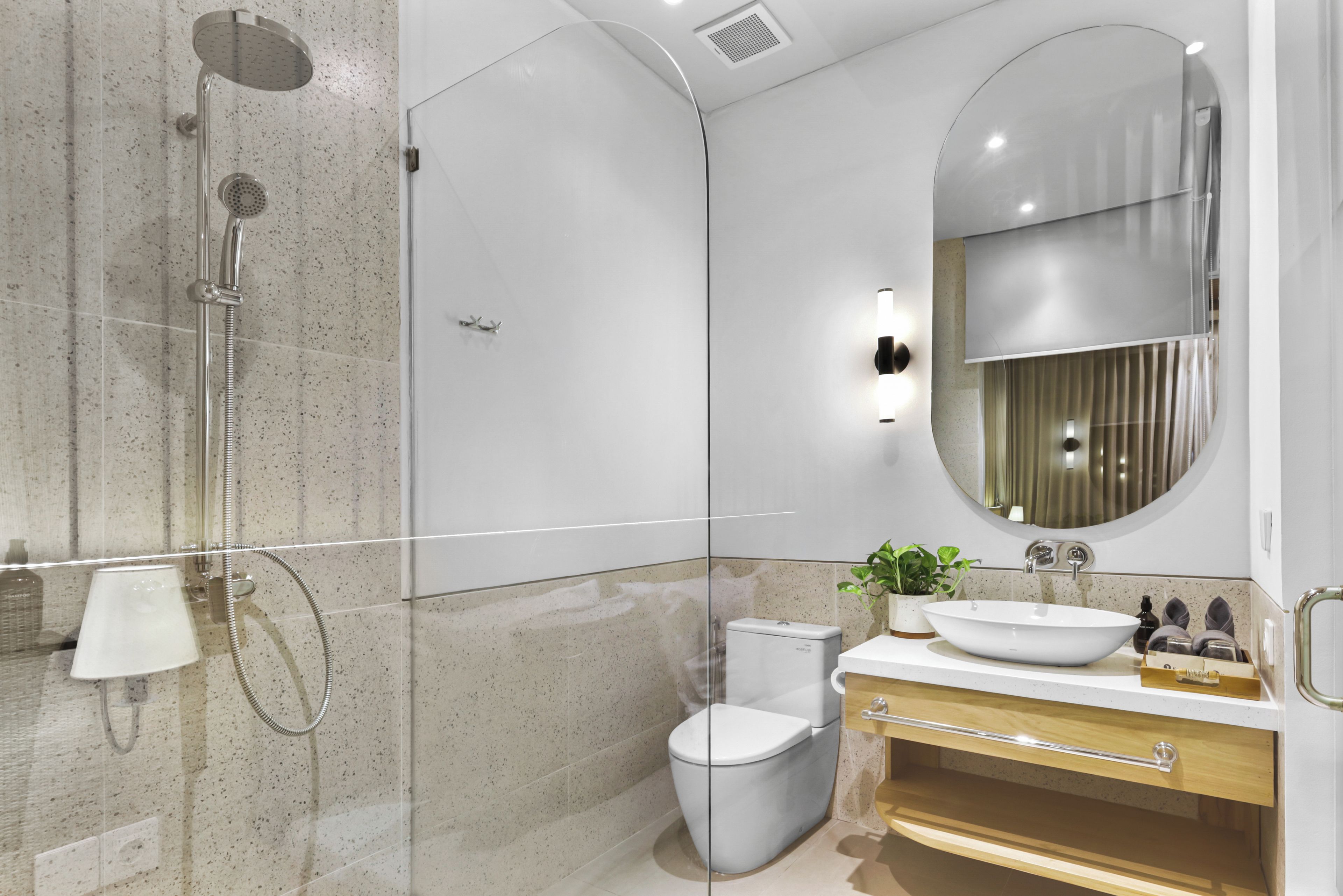 Un baño moderno con ducha de vidrio, inodoro, lavabo con espejo y una planta en el tocador.