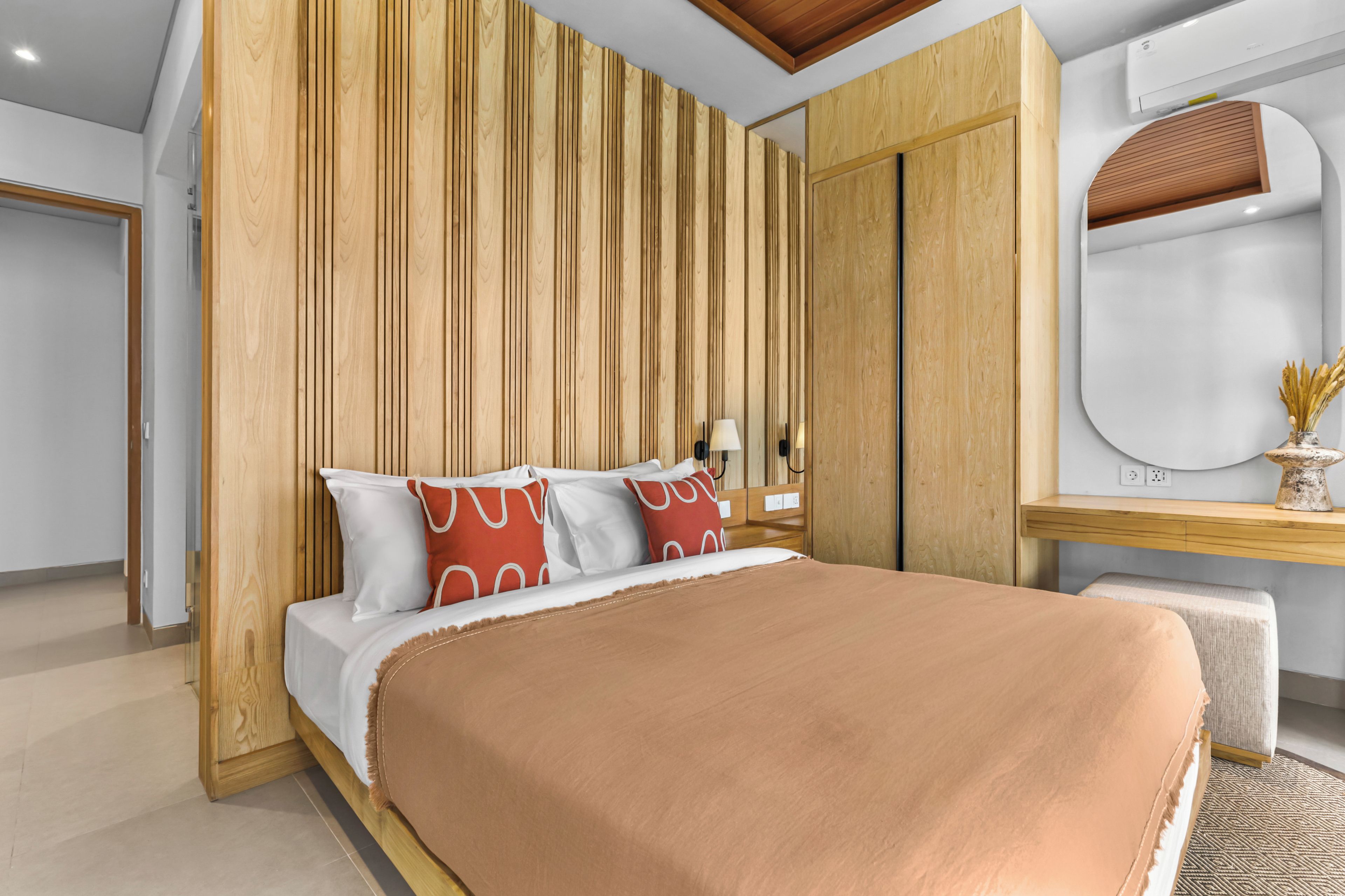 A modern bedroom with a wooden panel wall, a bed with white and red pillows, and a bedside table with a lamp.