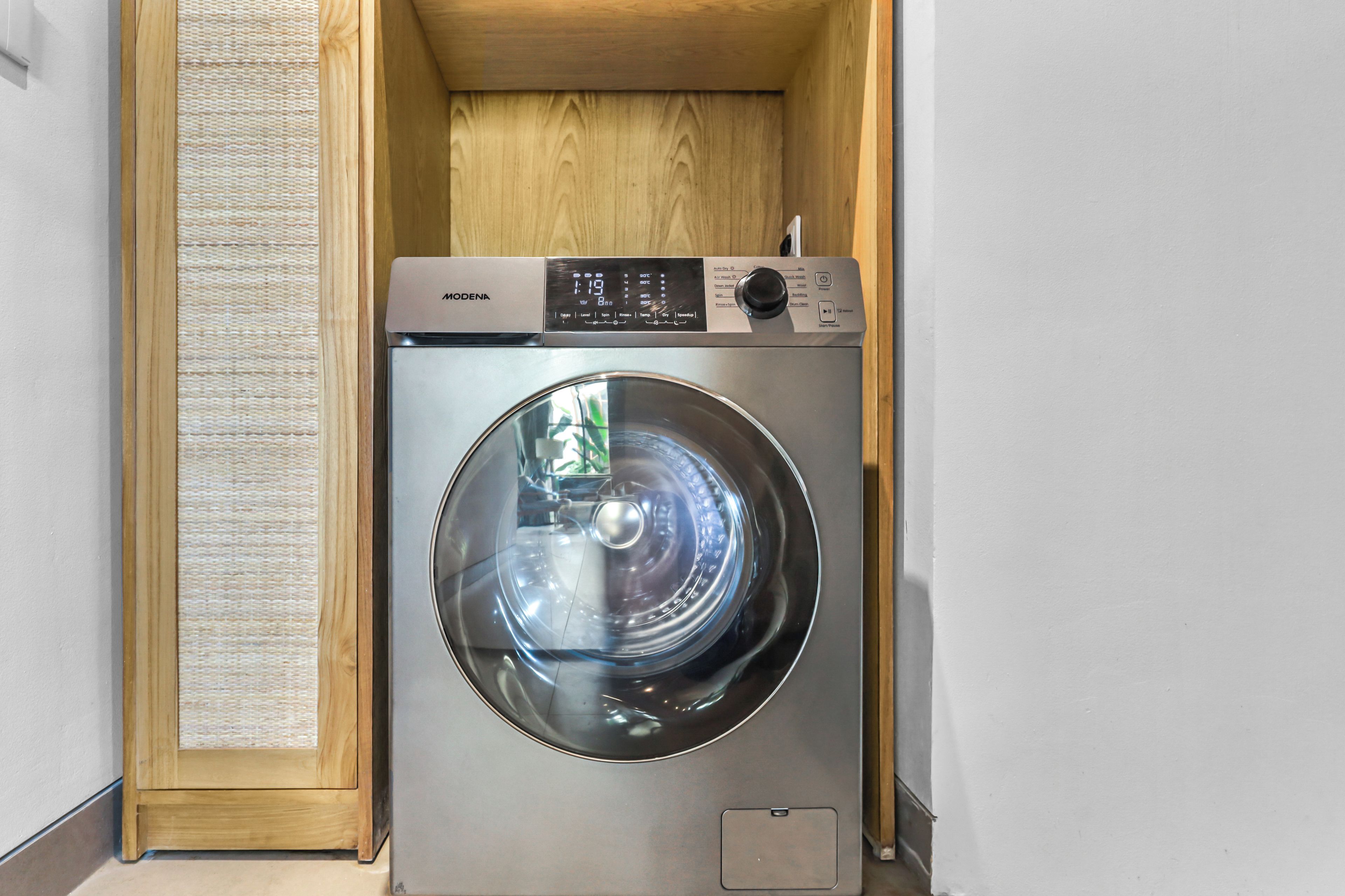 Een voorlader wasmachine in een houten kast, met een bedieningspaneel en een digitaal scherm.
