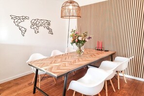 A dining area with a wooden herringbone table, white chairs, a hanging light fixture, and a wall-mounted plant. - VL19 Holiday home Zuidkust Vlissingen (Vlissingen)