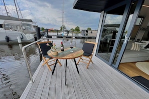 A wooden deck with a round table and chairs, a bottle of wine, and a glass of wine.
