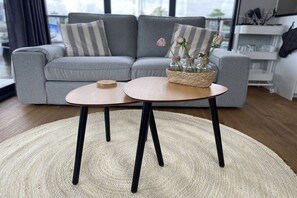 A modern living room with a grey sofa, a round coffee table with black legs, and a woven basket with flowers.