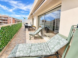 Ein Balkon mit Tisch und Stühlen, einer Liege und einer Glastür zu einem Innenbereich.