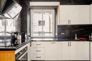 A modern kitchen with a black marble backsplash, white cabinets, and a window with blinds. - The Zahra Collection: Newly Renovated  Luxury 2 Bedroom Marina&Spain Views (Tanger)