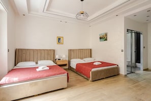 A hotel room with two beds, a wooden headboard, a red blanket, a painting, and a glass shower door. - The Zahra Collection: Newly Renovated  Luxury 2 Bedroom Marina&Spain Views (Tanger)