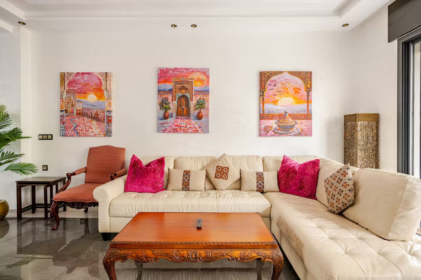 Una sala moderna con un sofá color beige, cojines decorativos, una mesa de centro de madera y tres obras de arte enmarcadas en la pared.