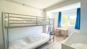 Une chambre avec un lit superposé, un bureau et une chaise, un berceau et une fenêtre avec des rideaux.