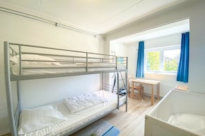 Ein Schlafraum mit Etagenbetten, einem Schreibtisch, einem Stuhl, einem Babybett und einem Fenster mit Vorhängen.