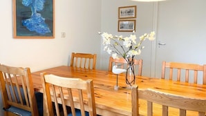 Un coin repas avec une table en bois, des chaises, un vase de fleurs et un tableau accroché au mur.