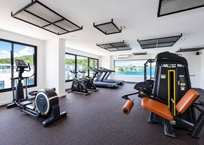 Un gimnàs amb màquines cardiovasculars, equip d'entrenament amb peses i grans finestres que donen vista a un paisatge urbà.