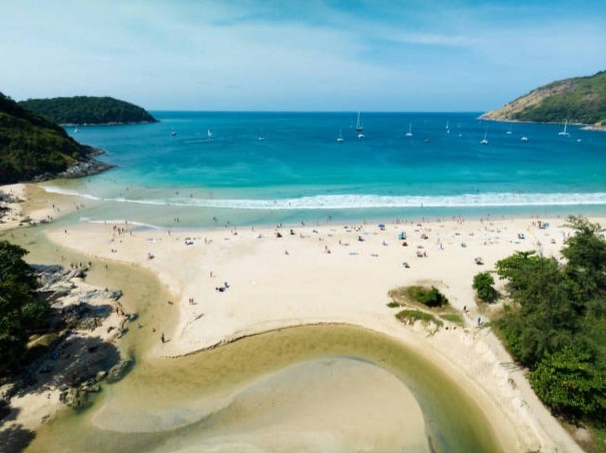 Une plage avec une eau cristalline, des bateaux et des gens.
