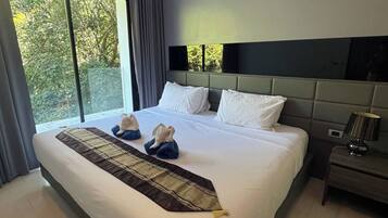A modern hotel room with a large bed, a nightstand with a lamp, and a view of trees through the window.