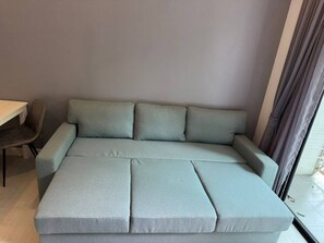 A grey sofa with a wooden table and a chair in a room with a grey wall and a window with curtains. - Utopia D Private & Quiet · 1BR · Pets OK · 500mbps (Rawai)