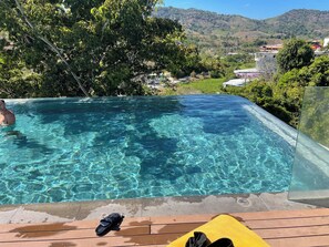 A clear swimming pool with a wooden deck and a yellow cushion, surrounded by lush greenery and a view of a hillside. - Utopia D Private & Quiet · 1BR · Pets OK · 500mbps (Rawai)