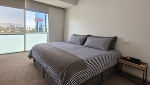 Een slaapkamer met een groot raam, een bed met geruit beddengoed en een nachtkastje.
