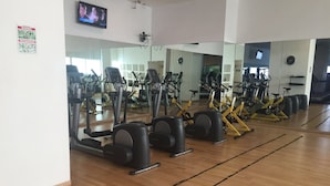 Een fitnessruimte met trainingsapparatuur, spiegels en een televisiescherm.
