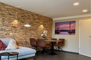 A modern living room with a stone wall, a dining area with chairs and a table, and a painting of a lighthouse. - Terrace apartment garden oasis (Lindau)