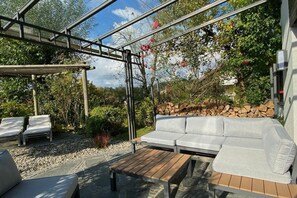 En utomhusplats med sittmöbler, bestående av en soffa och stolar, ett träbord och en pergola.