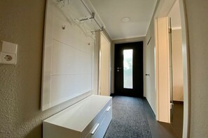 En hall med ett vitt skåp, en dörr längst ner och ett golv med en tydlig struktur.