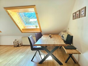 A room with a sloped ceiling, a wooden dining table, black chairs, and a view of greenery through a skylight. - Family Apartment No. 5 at Maierbauernhof Holiday Paradise (Bad Peterstal-Griesbach)