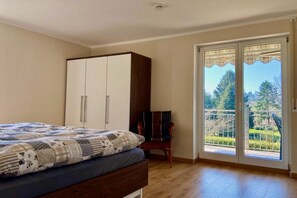 Ein Schlafzimmer mit Bett, Kleiderschrank, Sessel und einer Glastür zum Balkon.
