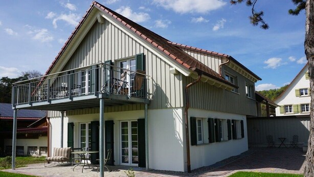 Une maison à deux étages dotée d’un balcon, d’une terrasse avec mobilier d’extérieur et d’une pelouse bien entretenue.