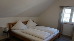 Un lit simple avec un cadre en bois, une literie blanche et une table de chevet avec une lampe.