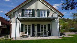 Un bâtiment à deux étages doté d’un balcon, d’un porche couvert et d’un petit espace extérieur aménagé pour s’asseoir.