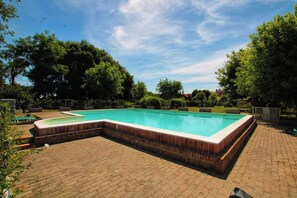 A rectangular swimming pool with a brick border, surrounded by a brick patio, and trees in the background. - Cozy studio apartment (40 square meters) with a pool in the Po Delta 1 (Veneto)