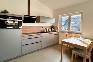 A modern kitchen with a built-in oven, a microwave, and a sink. There is a dining table with chairs and a window providing a view of the outside. - Schottenhof Walser 4 (Achberg)
