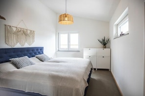 A bedroom with a large bed, a hanging light fixture, a window, and a plant on a shelf. - Schottenhof Walser 4 (Achberg)