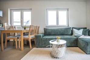A living room with a green sofa, wooden chairs, a round coffee table, and a window with blinds. - Schottenhof Walser 4 (Achberg)