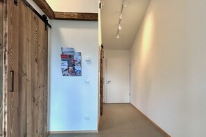 A hallway with a wooden door on the left, a poster on the wall, and a white door at the end. - Schottenhof Walser 4 (Achberg)