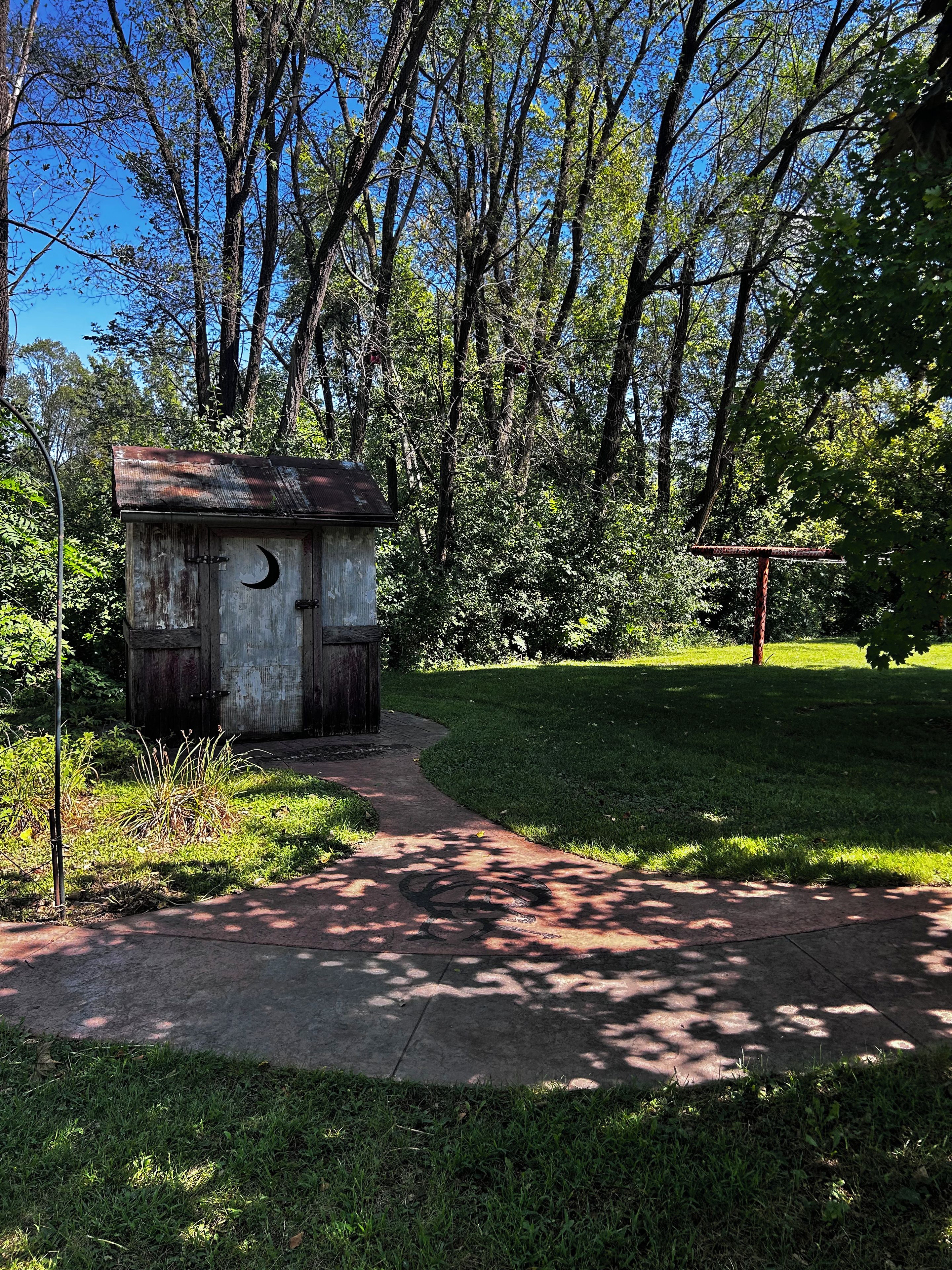 A rustic wooden structure with a crescent moon design, surrounded by lush greenery and a clear sky.