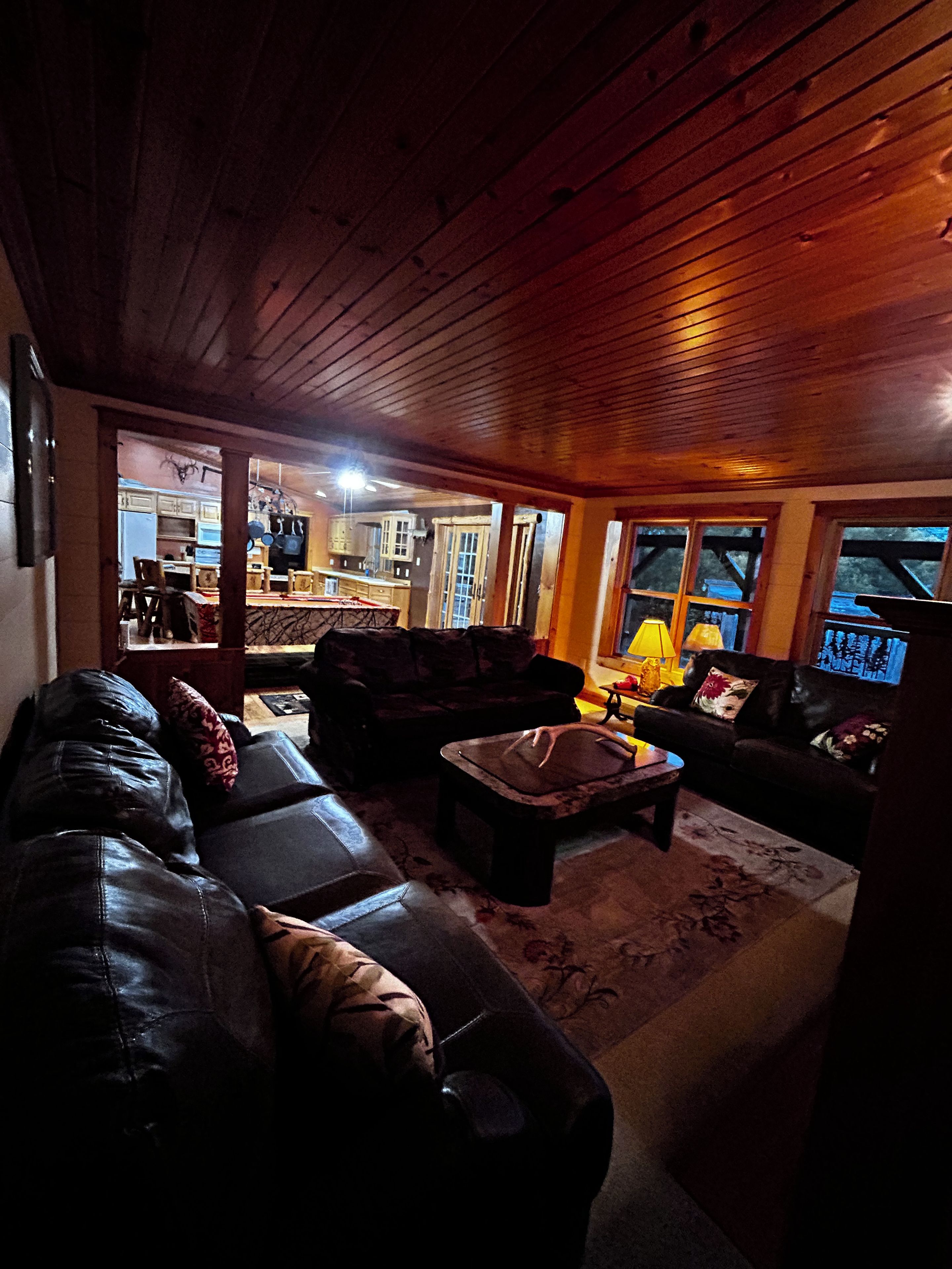 A cozy living room with a leather sofa, a coffee table, and a fireplace. There is a kitchen visible in the background.