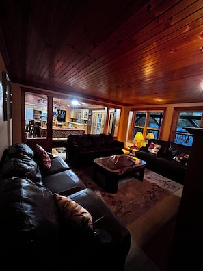 A cozy living room with a leather sofa, a coffee table, and a fireplace. There is a kitchen visible in the background.
