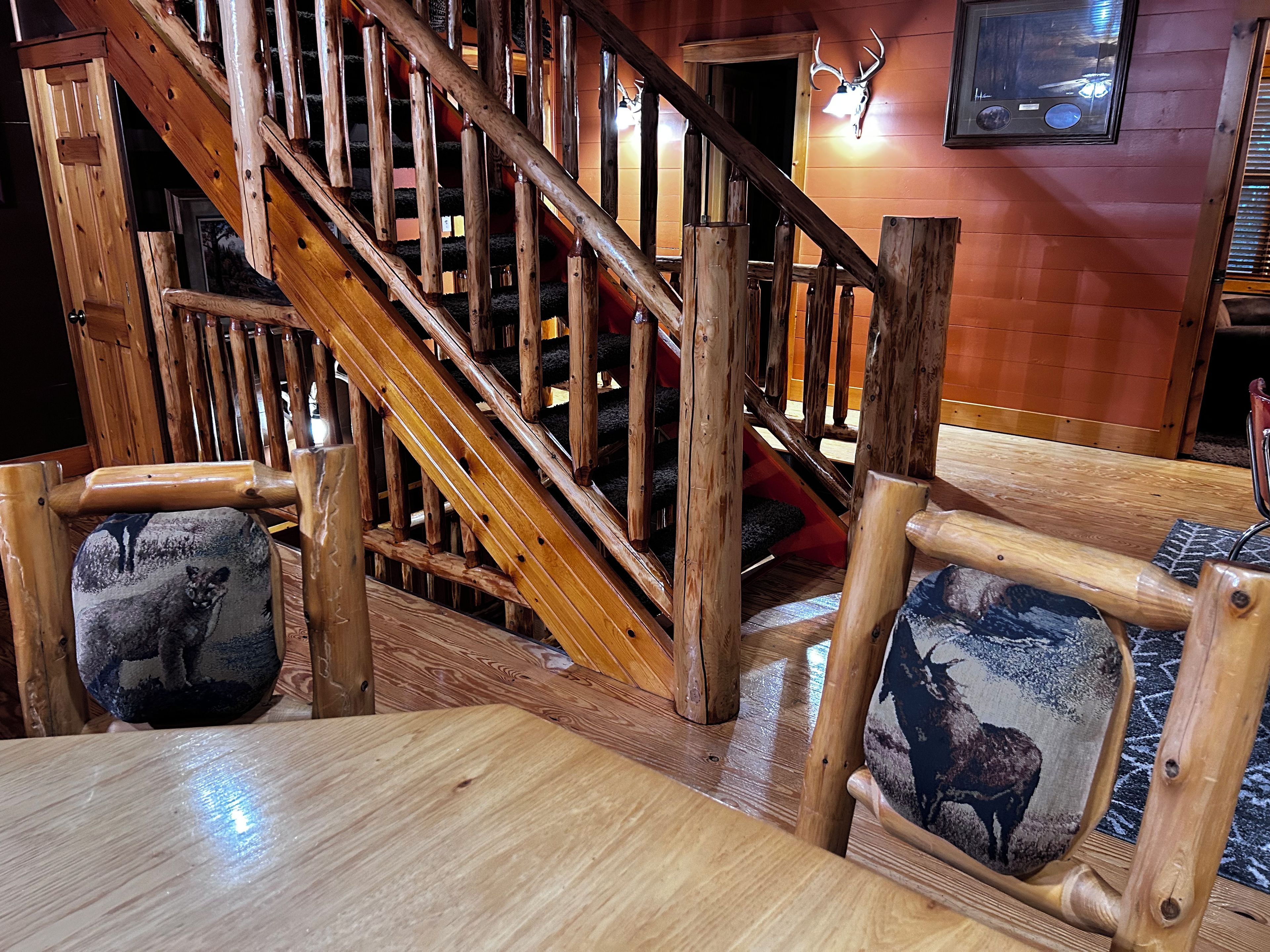 A wooden staircase with a red carpet, wooden railings, and a deer-patterned cushion on a wooden chair.