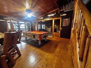 A wooden-floored room with a pool table, a ceiling fan, and fish mounted on the wall.