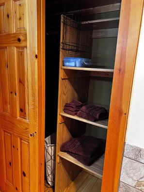 A wooden wardrobe with shelves, a hanging rack, and a small trash bin.