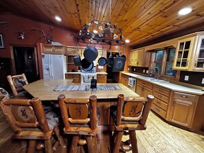 A wooden interior with a dining table surrounded by chairs, a hanging pot rack, and wooden cabinets.