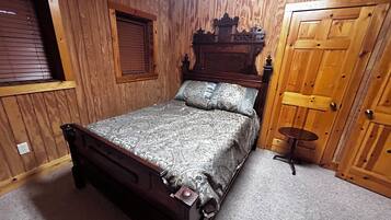 A bedroom with a wooden bed, a window with blinds, a wooden door, and a small round table.